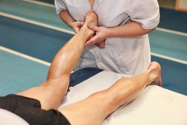 masseuse massaging athlete' s Achilles tendon after running